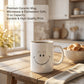 White 11oz ceramic mug showing both sides - hand-drawn smiley daisy flower and Your Smile Brightens The Day quote in blue script