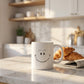 White 11oz ceramic mug showing both sides - hand-drawn smiley daisy flower and Your Smile Brightens The Day quote in blue script