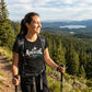 Woman hiking with poles and an 'Adventure' t-shirt in a scenic mountain landscape.